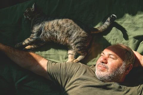 Top view of bearded middle-aged man lying on a bed and playing with his gra.. Stock Photos