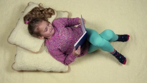 Top view of beautiful child with book lying on pillows Stock Footage 75587120
