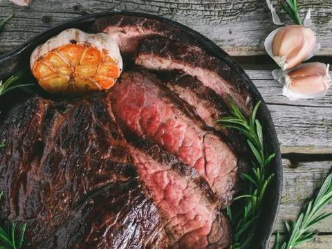 Top view of a beef steak medium rare with baked garlic and rosemary in a blac Stock Photos