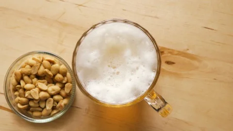 Top view of beer with foam and salty peanuts and on wooden table Stock Footage 115701348