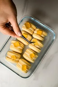 Top view of beige macaroons layer in a glass container, which a female hand 스톡 사진