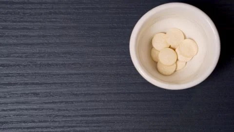 Top view. Beige tablets are falling from above into a white ceramic cup. Video stock 251857922