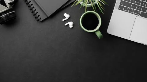 Top view of black desk with camera notebook earbuds green coffee cup laptop.. Stock Illustration