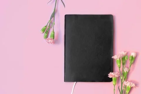 Top view of black empty book or notebook and flowers on pastel pink background Photos