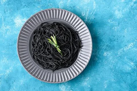 Top view black spaghetti with cuttlefish ink on grey plate with green leaf on Foto stock