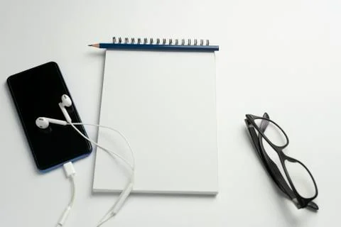 Top view of blank notebook , smartphone with earphones and glasses on white b Stock Photos
