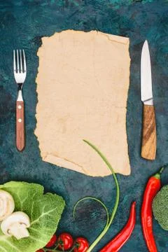 Top view of blank parchment, fork with knife and raw vegetables on black 库存照片
