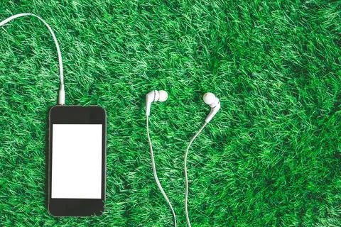 Top view of blank smart phone with earphones on green grass background. Stock Photos