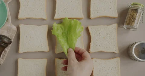 Top view of bread slices and hand putting green lettuce cooking saldwiches Video stock 236106844