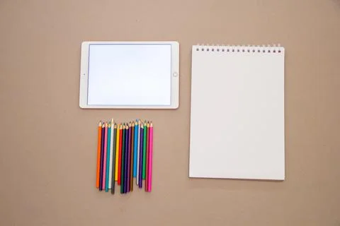 A top view of a bright screen of a tablet, empty notebook, and a set of sharp Stock Photos