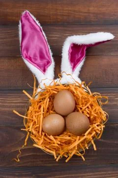 Top view brown eggs in a decorative nest with bunny ears on a wooden backgrou Stock Photos