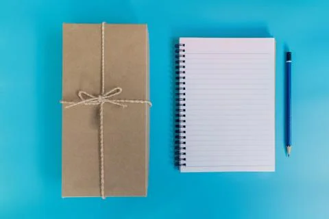 Top view brown gift box and notebook paper on blue pastel color background. Stock Photos