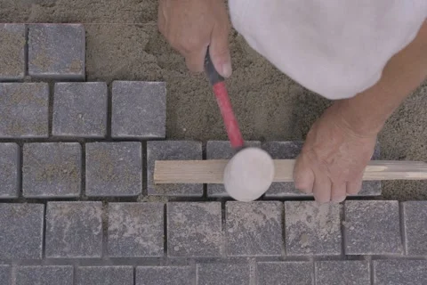 Top view of a builder leveling gray paving stones with a rubber mallet Stock Footage 345412432