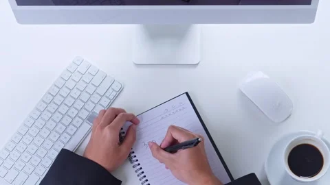 Top view of businessman writing notes in spiral notebook at clean white desk Stock Footage 328553361