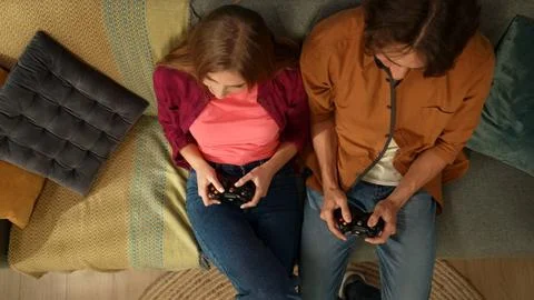 Top view capturing a young couple sitting on the couch, holding gamepads, acting Stock Photos