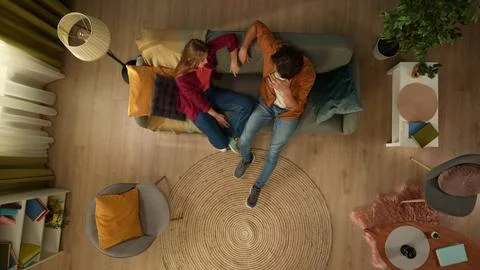 Top view capturing a young couple entering the frame. They sit on the couch Stock Photos