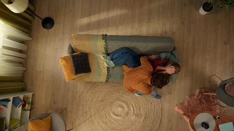 Top view capturing a young couple. The woman is laying on the couch, covering Stock Photos
