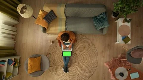 Top view capturing a young man sitting on the floor, looking at the laptop Stock Photos
