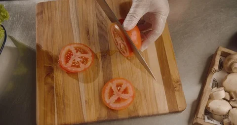 Top view chef cuts fresh tomato on slices with sharp knife on wooden board Stock Footage 113870004