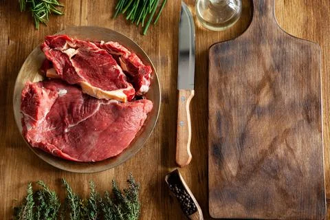 Top view of chef knife next to big chunks of red meat and green vegetables Foto stock