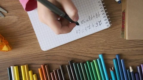 Top view of child doing math exercises in notebook with stationery on wooden Stock Footage 283763600
