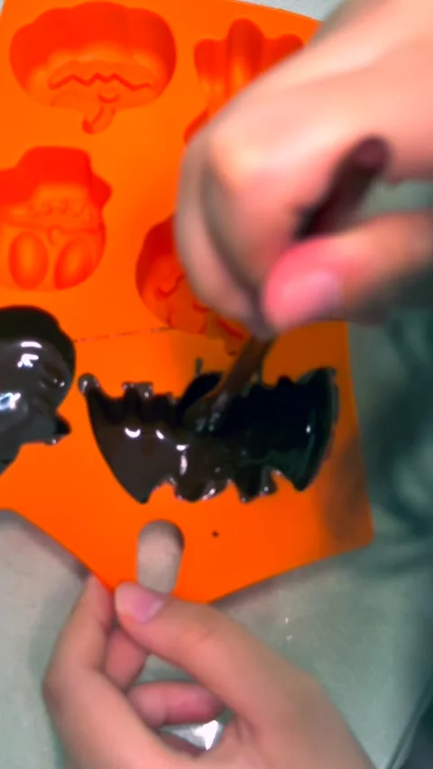 Top view of child hands filling bat-shaped mold with melted halloween chocolate Video stock 343477908