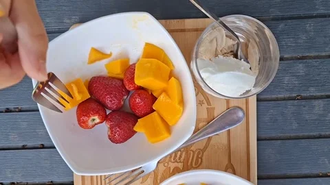 Top View of Child Picking Up Mango Piece with Fork from Fruit Bowl Outdoors Stock Footage 334699145