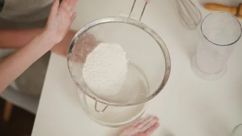 Top view of child tapping sieve while another person holds handle steady Stock Footage 307968378