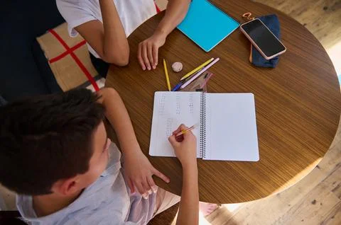 Top view of children doing homework at wooden table with notebooks Foto stock