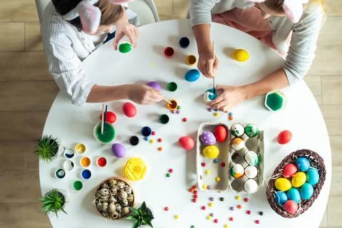 Top view, children at the table paint Easter eggs, paints, work atmosphere. Stock Photos