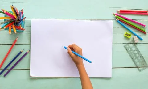 Top view of a child's hand using colored pencils drawn on white paper. Stock Photos