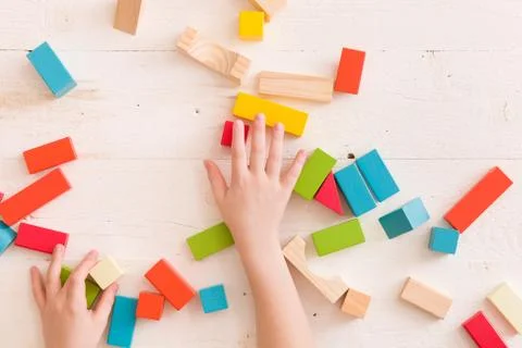 Top view on child's hands playing with colorful wooden bricks on the white ta Stock Photos