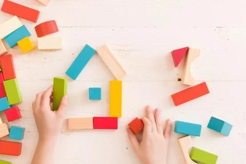 Top view on child's hands playing with colorful wooden bricks on the white ta Stock Photos