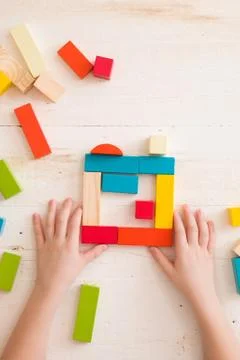 Top view on child's hands playing with colorful wooden bricks on white table  Stock Photos