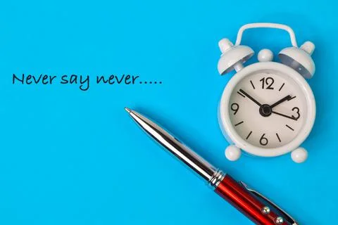 Top view of clock and pen over blue background written with NEVER SAY NEVER Stock Photos