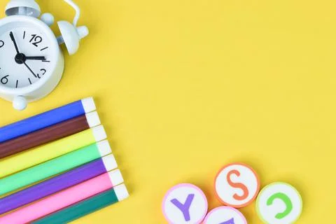 Top view of clock, pen colors and alphabet letters isolated on yellow backgro Stock Photos