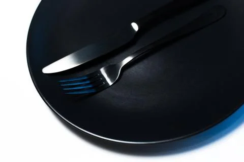 Top view close-up of black fork and knife on plate, isolated on white. Stock Photos