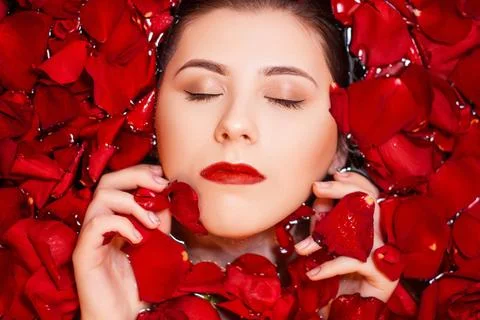 Top view, close-up face of a young woman in a bathtub full of red rose petals Stock Photos
