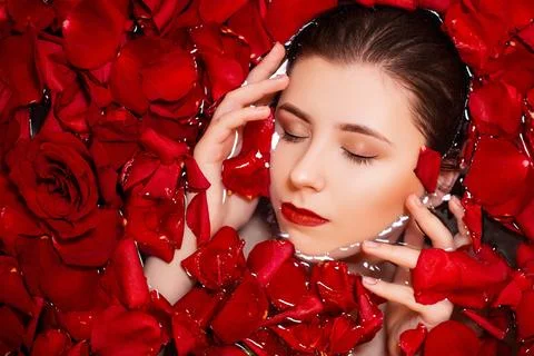 Top view, close-up face of a young woman in a bathtub full of red rose petals Stock Photos