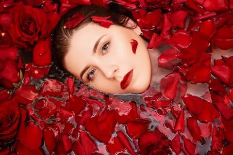Top view, close-up face of a young woman in a bathtub full of red rose petals Stock Photos