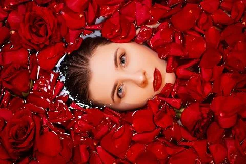 Top view, close-up face of a young woman in a bathtub full of red rose petals Stock Photos
