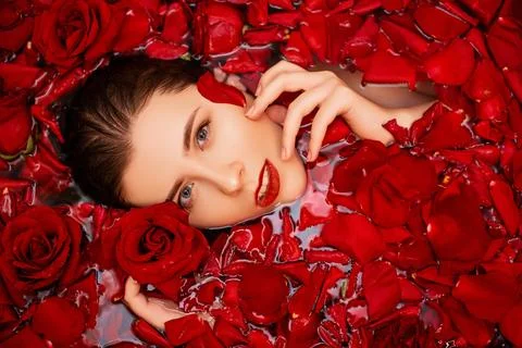 Top view, close-up face of a young woman in a bathtub full of red rose petals Foto stock