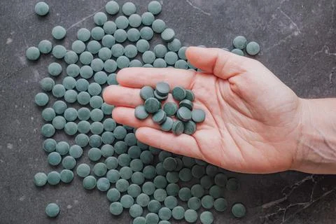 Top view close up of hand holding group of green spirulina tablets above ta.. Stock Photos