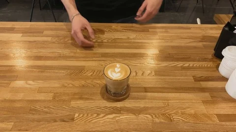 Top view. Close up of hand taking coffee of  cup on wood table. Coffee art latte 스톡 동영상 123553276