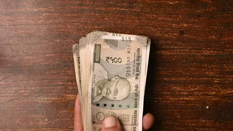 Top View Close-Up of a Man Placing 500/- Currency Note Bundles on Wooden Table Stock Footage 329353538