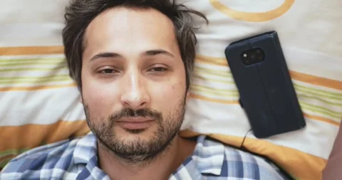 Top view close-up of a man sleeping and a smartphone lying on a pillow next to Stock Footage 260032227