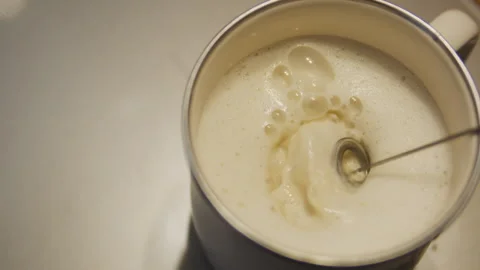 Top view close-up of milk frothing in metal cup on electric stove Stock Footage 331856323