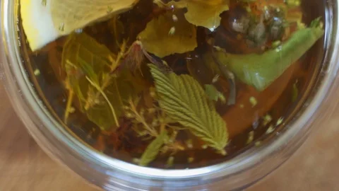 Top view close-up tea leaves opening in hot water at transparent cup. Brewing Stock Footage 126765785