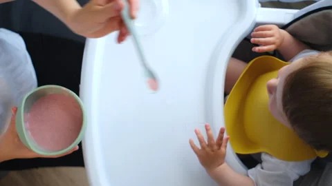 Top view close up of young mother feeding pretty baby from spoon Stock Footage 280180738
