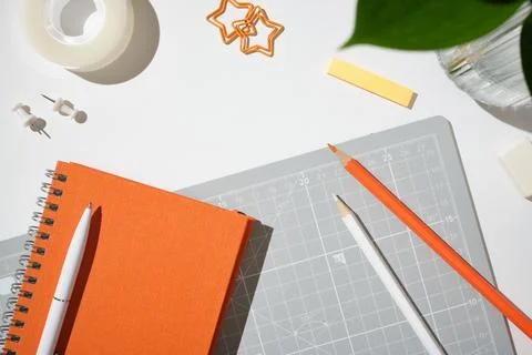 Top view of a closed orange notebook, white pen, cutting mat, and pencils o.. Stock-Fotos